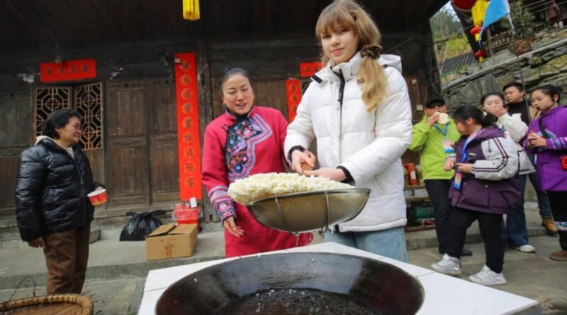 A scenic rural Chinese village with terraced fields and traditional homes attracting international travelers and online audiences.